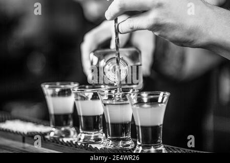 Aufnahmen im Nachtclub. Roter Cocktail im Nachtclub. Barkeeper bereitet Cocktail-Shooter. Barkeeper gießt starkes alkoholisches Getränk in kleine Gläser Stockfoto