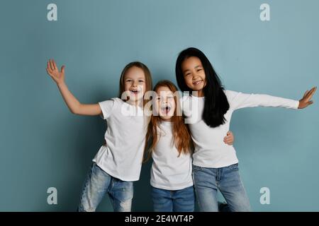 Fröhliche multirassische Mädchen Freunde in Jeans und weißen T-Shirts haben Spaß zusammen lachen spielen umarmt einander Stockfoto