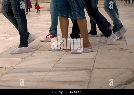 Eine Gruppe von jungen Besuchern, die zusammen auf weißem Marmorboden auf der Plattform des Taj Mahal mit Einweg-Socken auf. Stockfoto