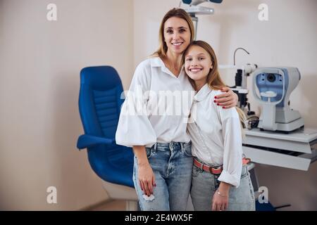 Glücklich lächelnde Frau und Teenager-Mädchen stehen vor Die andere moderne Maschine im Optikerzentrum Stockfoto
