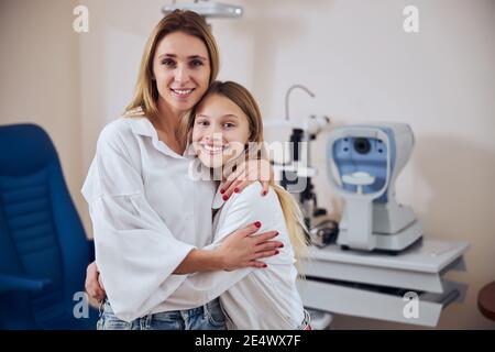 Glücklich lächelnde Mutter und Tochter posiert und Blick auf die Fotokamera im optometrischen Schrank Stockfoto