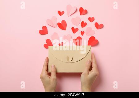 Weibliche Hände halten Umschlag auf rosa Hintergrund mit dekorativen Herzen Stockfoto