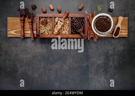 Grün und braun ungegeröstete und dunkel geröstete Kaffeebohnen in Holzkiste mit Kugeln auf dunklem Steinhintergrund. Stockfoto