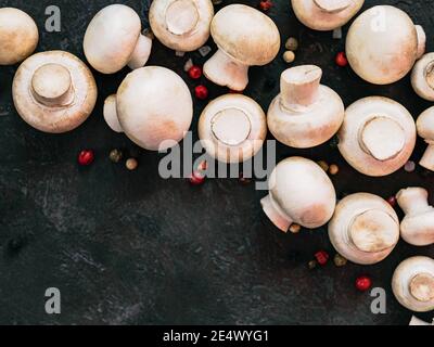 Mini-Champignons mit Kopierplatz am linken Rand. Rohe ganze Pilze auf schwarzem Hintergrund, Kopierraum. Ansicht von oben oder flach liegend. Stockfoto