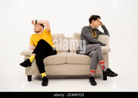 Zwei gutaussehende Jungs hatten einen Kampf, während sie auf den gegenüberliegenden Seiten des Sofas saßen. Eine Gruppe von Freunden sitzt auf einer weichen Couch und kommuniziert isoliert Stockfoto