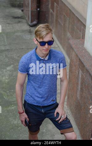 Blick von oben auf einen Winkel von jungen Mann in blauem Hemd und Shorts mit Smartphone in der Hand zu Fuß die Treppe hinauf. Blonde Mann trägt Sonnenbrille ist h Stockfoto