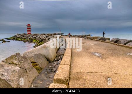 Betonsteg in der Nähe von IJmuiden mit Angler Fischer an einem bewölkten Nachmittag. Provinz Nordholland, Niederlande Stockfoto