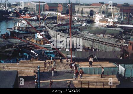 Ein Blick auf die geschäftigen Hafenaktivitäten an der Uferpromenade des Hafenviertels von La Boca, Buenos Aires, Argentinien im Jahr 1962. Hier wird Holz von Hafenarbeitern aus dem Schiff im Vordergrund entladen. Als eines der 48 ‘Barrios’ (Viertel) der Hauptstadt liegt La Boca im Südosten der Stadt. Es behält einen starken italienischen Geschmack, mit vielen seiner frühen Siedler aus der Stadt Genua. Stockfoto