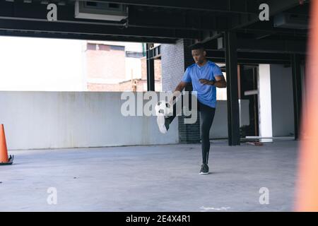 afroamerikanischer Mann macht Tricks mit einem Fußball in leer Stadtgebäude Stockfoto