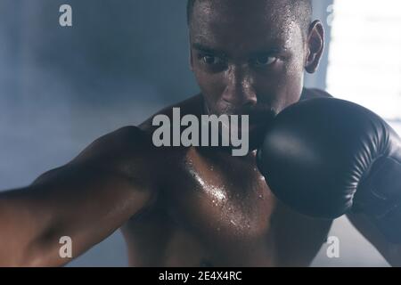 Afroamerikanischer Mann trägt Boxhandschuhe Boxsack Boxsack boxing in Ein leeres Stadtgebäude Stockfoto