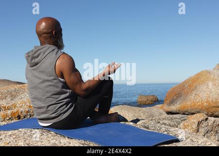 Fit Senior african american Mann sitzt auf felsigen Küste meditieren. Gesunde Ruhestand Outdoor Fitness-Lifestyle. Stockfoto