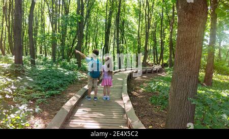 Kinder folgen einem Wanderweg auf einer gut ausgestatteten Holzplankenstraße in einem Naturschutzgebiet. Umweltschutzkonzept. Der Junge hält seine Freundin Stockfoto