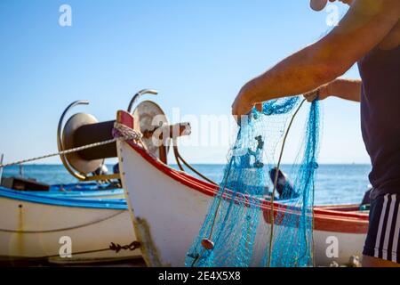 Fischer häufen Fischnetz und bereiten sich auf sein nächstes Angeln. Die Boote sind trocken am Sandstrand angedockt. Stockfoto