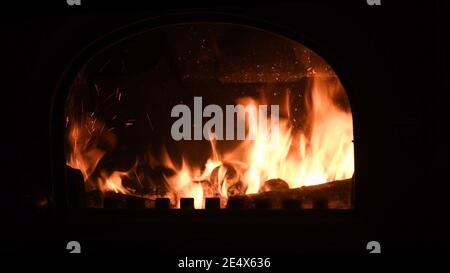 Retro-Kamin mit brennenden Feuerholz und glühende Flamme im Inneren mit hellen Funken. Gemütliches warmes Licht in der Dunkelheit der Nacht. Romantischer Hintergrund für den Winter Stockfoto