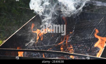 Feuer brennt im Grill mit altem Metallgitter mit Asche und grauem fliegenden Rauch. Flammen und Rauch aus rustikalem mangal im Freien Stockfoto