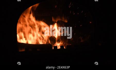 Entkochte Kamin mit brennendem Brennholz und glühende Flamme im Inneren mit hellen Funken. Gemütliches warmes Licht im Ofen bei Dunkelheit. Natürliches feuriges Bac Stockfoto