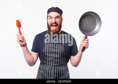 Foto des staunenden Küchenchefs mit leerer Bratpfanne und Utensilien. Stockfoto