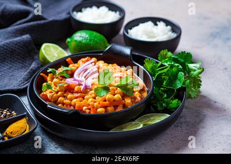 Veganes Kichererbsen-Curry mit Reis und Koriander in einer schwarzen Schüssel, dunkler Hintergrund. Konzept der indischen Küche. Stockfoto