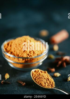 Indische oder pakistanische Masala Pulver in Löffel und Glas. Hausgemachte trockene Curry Garam Masala Mischung Gewürze Mischung auf dunkelgrauen und blauen Hintergrund. Vertikal Stockfoto