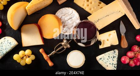 Käse- und Weinpanorama, verschiedene Käsesorten, aufgenommen von oben auf dunklem Hintergrund mit Trauben Stockfoto