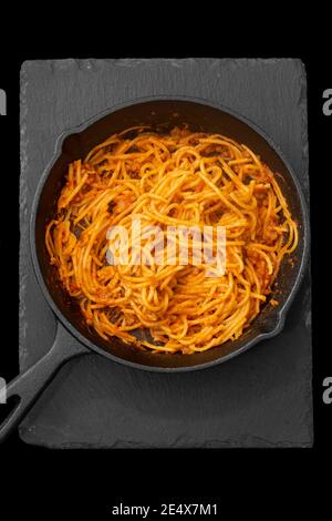 Spaghetti Bolognese in einer gusseisernen Pfanne gekocht. Auf schwarzem Hintergrund Stockfoto
