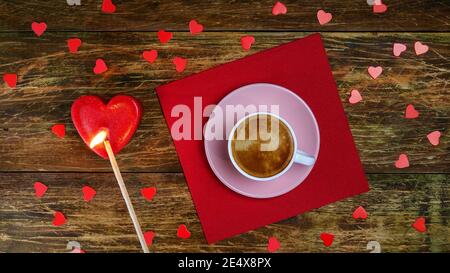 Tasse Kaffee auf roter Serviette und zünden herzförmige Kerze mit langem Streichholz an. Ein romantischer Tag. Valentinstag oder Frauentag Konzept. Draufsicht. Flach liegend Stockfoto