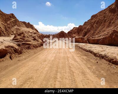 Endlose sandige Straße umgeben von rauen Felsen unter blauem Himmel An sonnigen Tagen in der Atacama Wüste Stockfoto