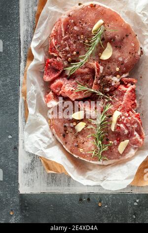 Zwei rohe Schweinesteaks grauen Stein Hintergrund mit Rosmarin und Gewürzen. Draufsicht, Kopierbereich. Stockfoto