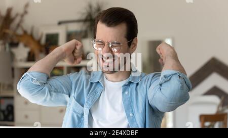 Aufgeregter junger Mann, der beide Fäuste stolz auf den Sieg hochhebt Stockfoto