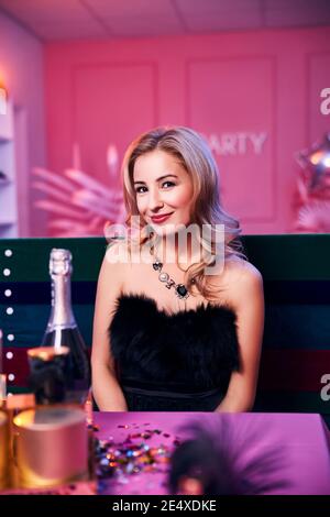 Lächelnde blonde junge Frau sitzt am festlichen Tisch Stockfoto