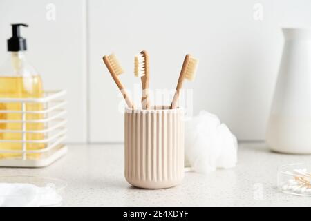 Keramikbecher mit Bambuszahnbürsten in der Nähe des Schwamms Und verschiedene Hygieneartikel auf Regal in hellen Badezimmer Stockfoto