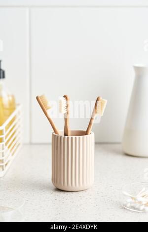 Becher mit sauberen Bambuszahnbürsten für die Mundpflege aufgelegt Marmorregal an der gefliesten Wand am Morgen in der Toilette Zu Hause Stockfoto