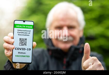 Älterer Mann zeigt einen Gesundheitsausweis auf einem Handy, was auf eine Impfung gegen covid-19 hinweist. Stockfoto