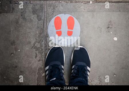 Stand über Covid 19 Einschränkungen Schild bleiben zwei Meter auseinander Soziale Distanzierung mit Schuhen im Bild rote Fußtreppen Lockdown 2 Warten Sie hier Coronavirus Stockfoto