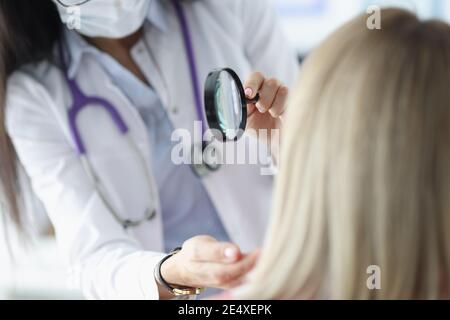 Dermatologe untersucht das Gesicht des Patienten durch eine Lupe Stockfoto
