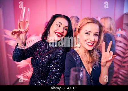 Fröhliche Frau mit einem Sektglas und Blick auf ihre Freundin Stockfoto