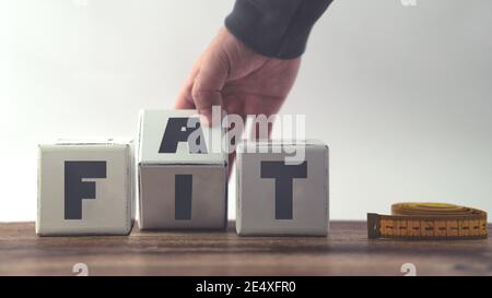 Menschliche Hand dreht Holzwürfel vom FETT zum EINPASSEN. Spiegeln Holzwürfel mit Text Diät Gewicht zu verlieren Konzept Stockfoto