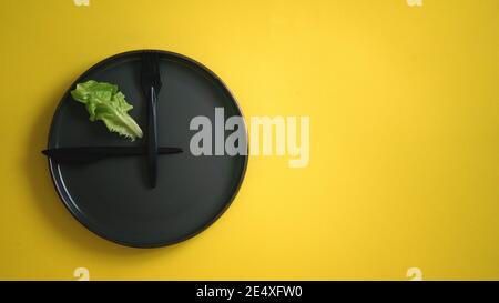 Blick von oben auf frischen grünen Salatblatt auf einem schwarzen Teller mit Gabel und Messer wie eine Uhr Für Ernährung Konzept gesunde Lebensweise intermittierende fa Stockfoto