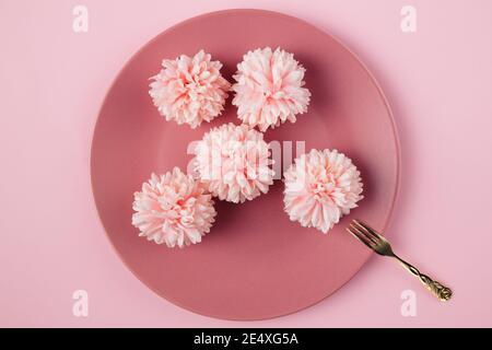 Draufsicht auf fünf Blüten mit Goldgabel in der Platte vor rosa Hintergrund. Flach liegend Stockfoto