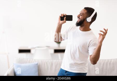 Afrikanischer Mann Singing Song Holding Telefon Wie Mikrofon Zu Hause Stockfoto