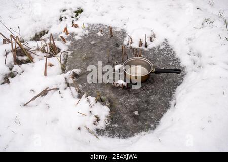 Ein Loch im Eis in einem gefrorenen Garten machen Wildtierteich im Winter, indem eine Pfanne mit Kochendes Wasser darin auf dem eisigen Teich Stockfoto