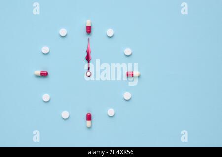 Uhr aus Pillen und Kapseln auf pastellblauem Hintergrund erstellt. Richtige Zeit für die Verwendung von Medikamenten. Flaches Lay. Stockfoto