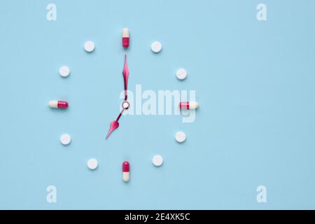 Uhr aus Pillen und Kapseln auf pastellblauem Hintergrund erstellt. Richtige Zeit für die Verwendung von Medikamenten. Flaches Lay. Stockfoto