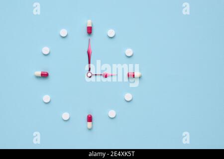 Uhr aus Pillen und Kapseln auf pastellblauem Hintergrund erstellt. Richtige Zeit für die Verwendung von Medikamenten. Flaches Lay. Stockfoto