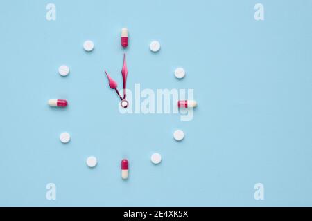 Uhr aus Pillen und Kapseln auf pastellblauem Hintergrund erstellt. Richtige Zeit für die Verwendung von Medikamenten. Flaches Lay. Stockfoto