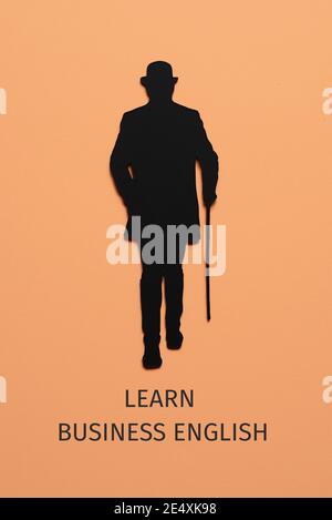 Die Silhouette eines eleganten Mannes, mit Hut und mit einem Gehstock, Ausschnitt auf einem schwarzen Karton, und der Text sprechen Business-englisch auf einem blassen oder Stockfoto