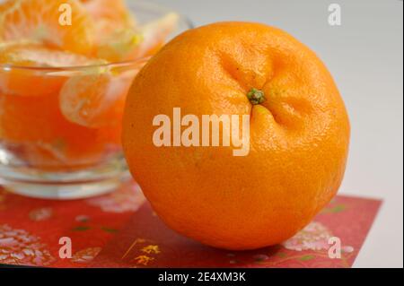 Nahaufnahme der Mandarin Orangen (Lukan) und geschälte Segmente in einer Glasschüssel mit roten Umschlagspaketen Stockfoto