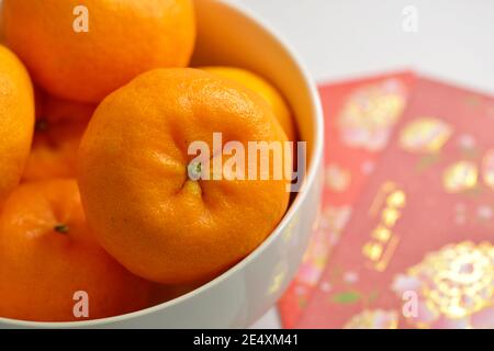 Nahaufnahme der Mandarinen Orangen (Lukan) in einer weißen Schale und roten Hüllpackungen vor weißem Hintergrund Stockfoto