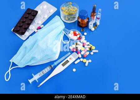 Medizinische Schutzmaske mit Pillen, Thermometer, Medikamente, Spritzen auf blauem Schreibtisch. Gesundheitskonzept und medizinisches Konzept. Stockfoto