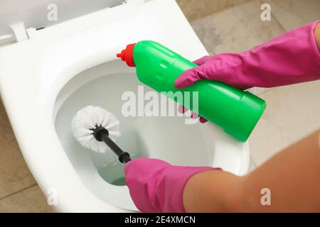 Frau in Gummi rosa Handschuhe reinigt Toilettenschüssel mit Pinsel Stockfoto